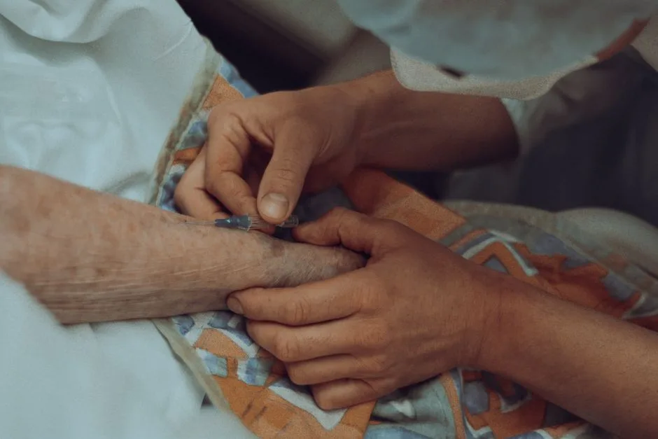 Caregiver's hand supporting an elderly patient's arm with an IV