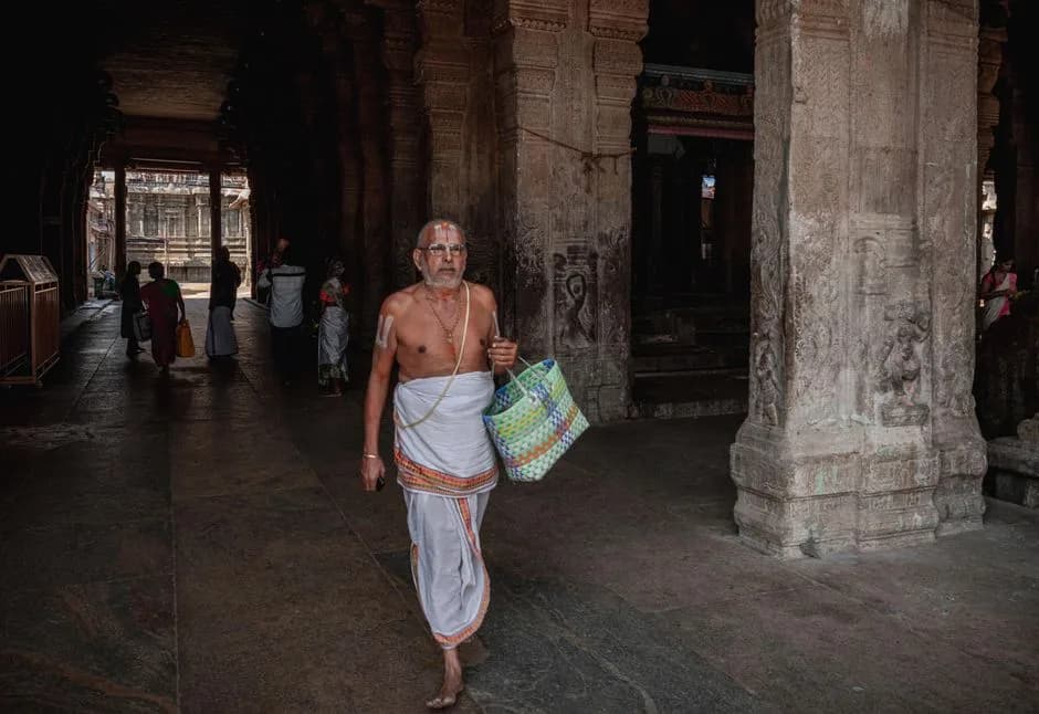 Elderly Indian man in traditional attire walking through a temple corridor