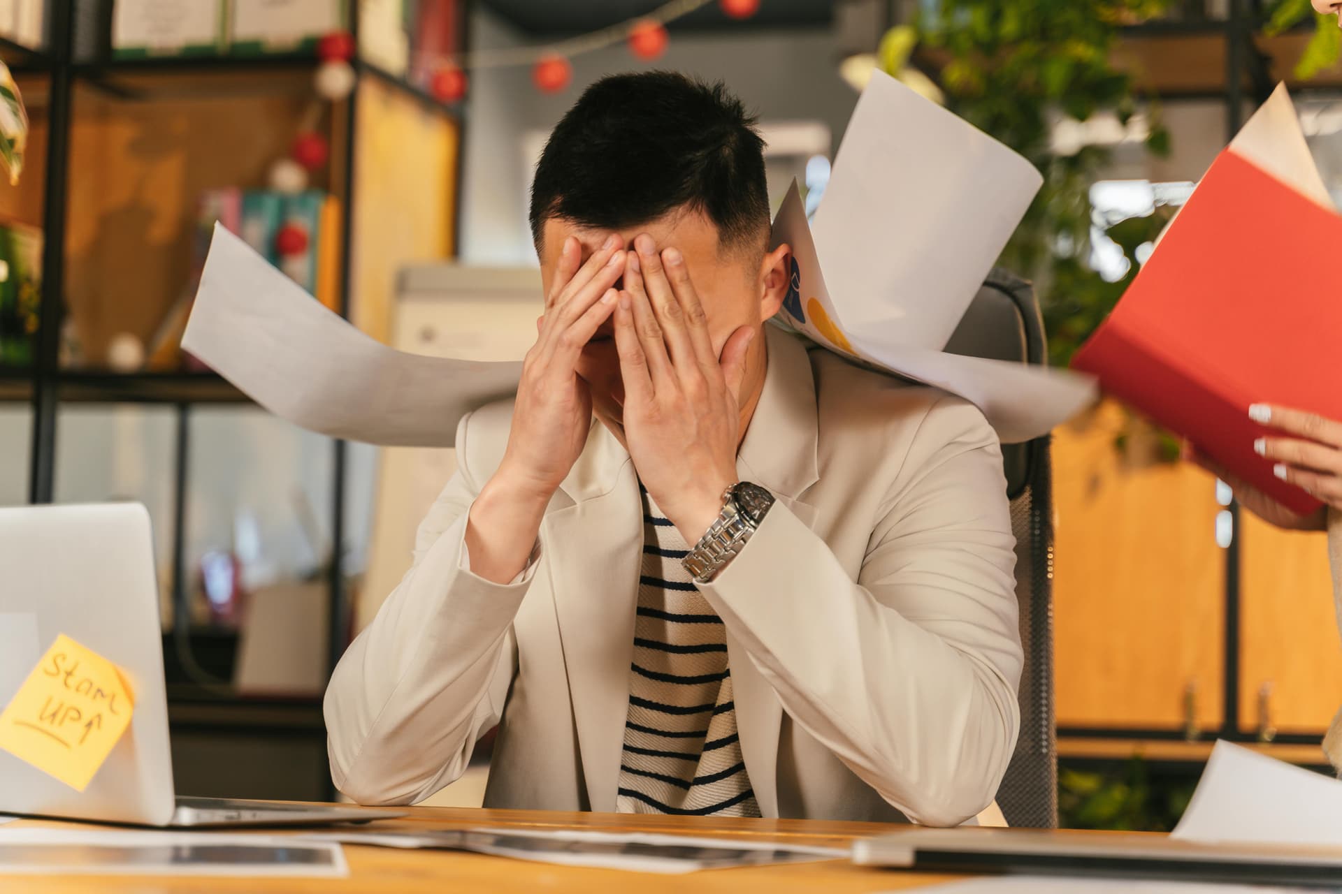 An exhausted adult child sitting at a desk, managing multiple medical forms and calls, visibly stressed